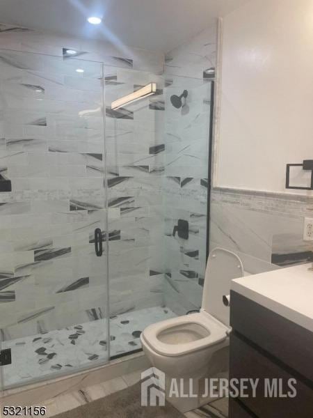 bathroom featuring vanity, toilet, tile walls, and a shower with shower door