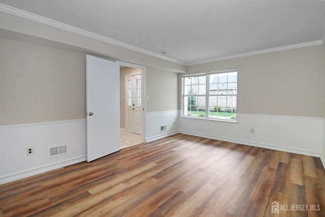 empty room with wood finished floors, crown molding, and a wainscoted wall