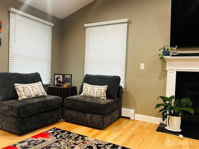 sitting room featuring lofted ceiling, a baseboard heating unit, baseboards, light wood-style floors, and a fireplace