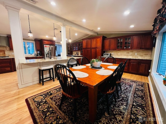 dining room featuring light wood finished floors, lofted ceiling, ornate columns, and recessed lighting
