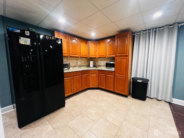 kitchen featuring stainless steel microwave, brown cabinetry, black refrigerator with ice dispenser, recessed lighting, and light stone countertops