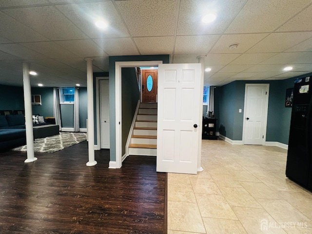 finished below grade area featuring baseboards, stairs, light wood finished floors, and a paneled ceiling