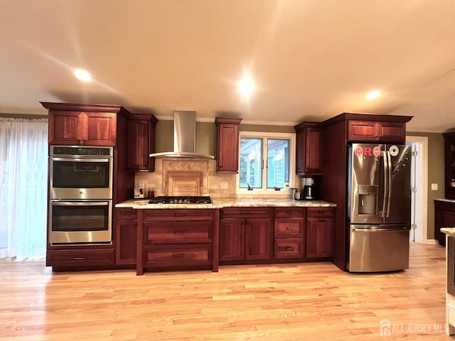 kitchen featuring stainless steel appliances, light wood-type flooring, light stone counters, wall chimney range hood, and tasteful backsplash