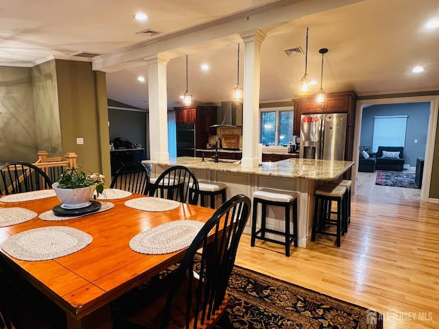 dining space with light wood finished floors, vaulted ceiling, visible vents, and ornate columns