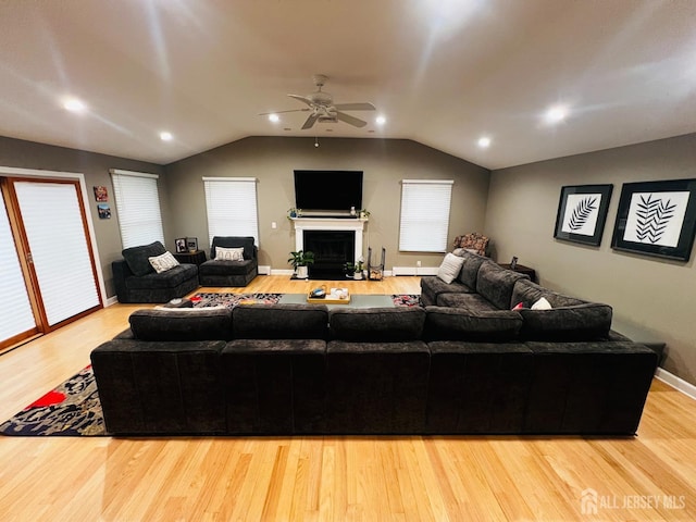 living area featuring wood finished floors, vaulted ceiling, ceiling fan, a fireplace, and baseboards