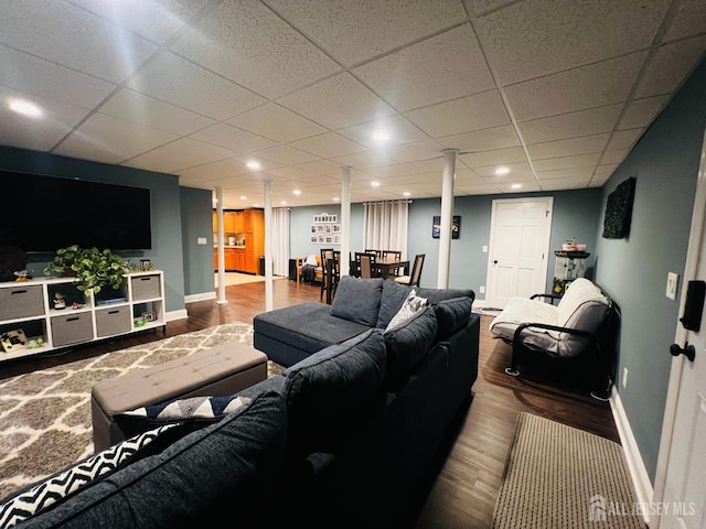 living area featuring baseboards, a drop ceiling, and wood finished floors