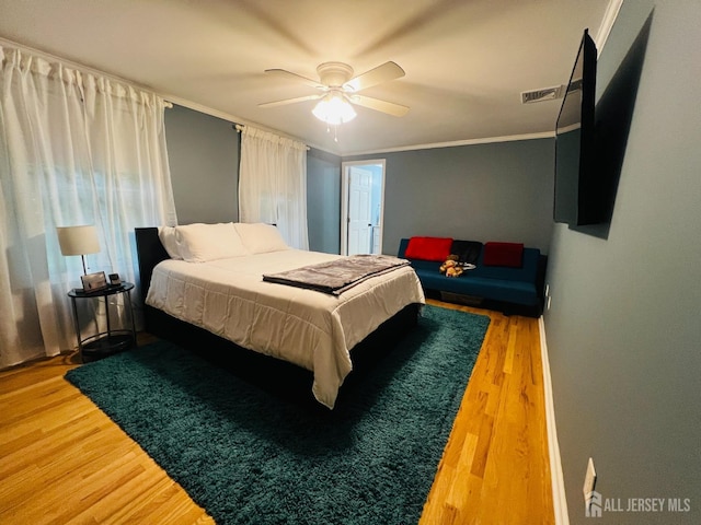 bedroom featuring ceiling fan, ornamental molding, visible vents, and wood finished floors