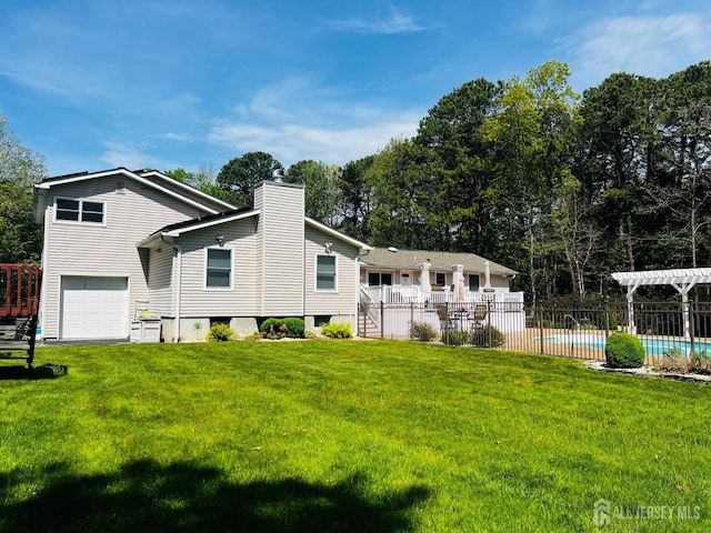back of house with fence, an attached garage, a yard, a fenced in pool, and a chimney