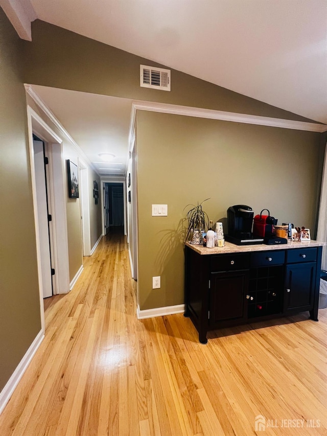 hall featuring light wood-type flooring, visible vents, baseboards, vaulted ceiling, and ornamental molding