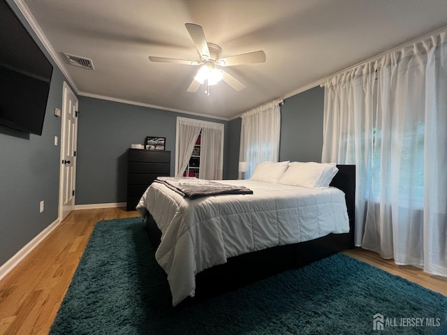 bedroom with light wood finished floors, a ceiling fan, crown molding, visible vents, and baseboards