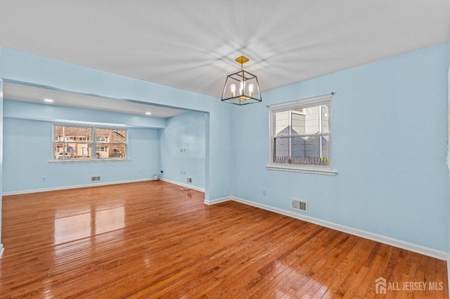 empty room with visible vents, an inviting chandelier, baseboards, and hardwood / wood-style flooring