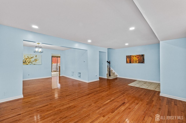 unfurnished living room featuring recessed lighting, stairway, wood-type flooring, and baseboards