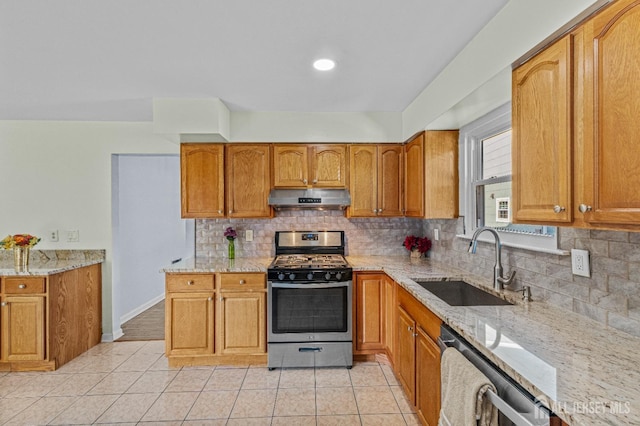 kitchen with under cabinet range hood, light stone counters, a sink, stainless steel appliances, and light tile patterned flooring