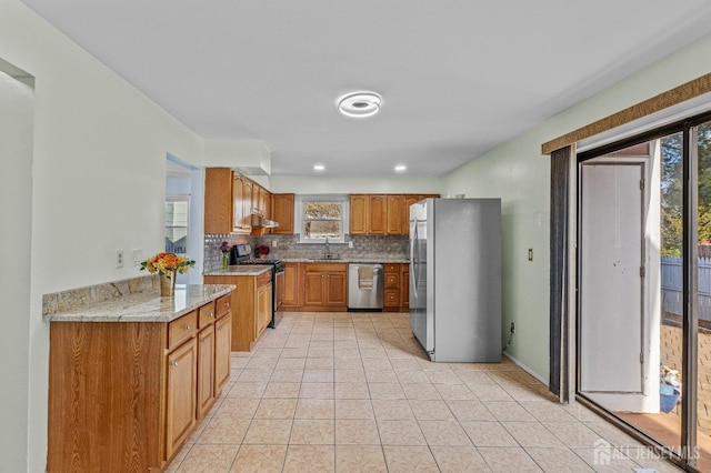 kitchen with a sink, backsplash, stainless steel appliances, brown cabinetry, and light tile patterned floors