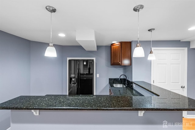 kitchen featuring a peninsula, a sink, black fridge, brown cabinetry, and pendant lighting