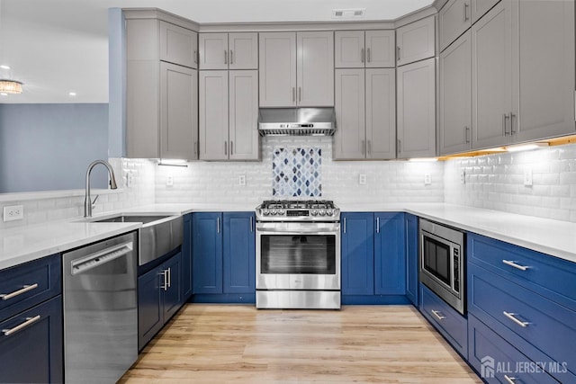 kitchen featuring under cabinet range hood, blue cabinetry, stainless steel appliances, and a sink