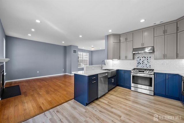 kitchen featuring blue cabinets, a peninsula, stainless steel appliances, light wood-type flooring, and under cabinet range hood