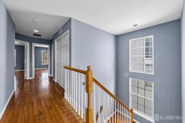 hall featuring wood-type flooring, visible vents, baseboards, and an upstairs landing