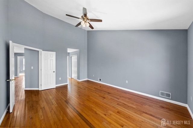 interior space featuring a high ceiling, a ceiling fan, visible vents, baseboards, and wood-type flooring