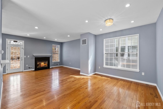 unfurnished living room featuring baseboards, a fireplace with flush hearth, visible vents, and light wood-style floors