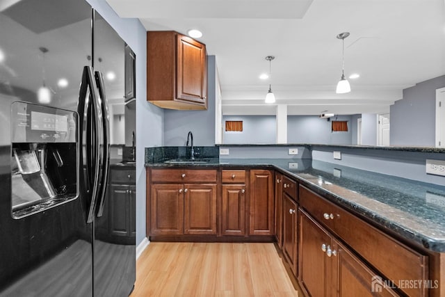 kitchen with dark stone counters, black fridge with ice dispenser, light wood-style flooring, pendant lighting, and a sink