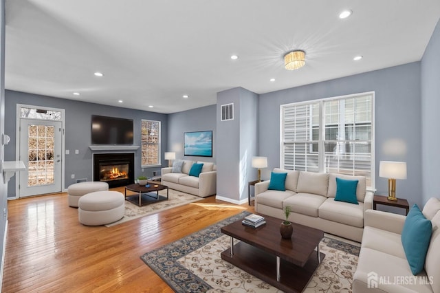 living area featuring hardwood / wood-style flooring, plenty of natural light, a glass covered fireplace, and visible vents