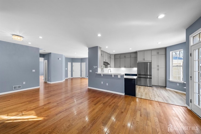 kitchen featuring gray cabinets, light countertops, visible vents, freestanding refrigerator, and under cabinet range hood