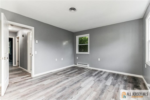 spare room featuring baseboards, wood finished floors, visible vents, and a baseboard radiator