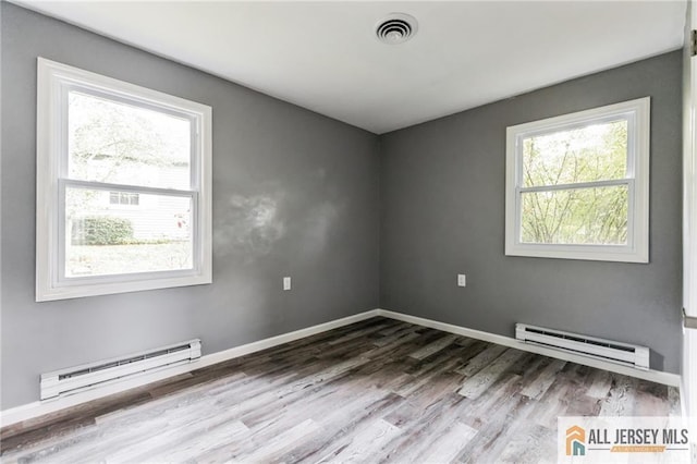 empty room with visible vents, a baseboard heating unit, baseboards, wood finished floors, and a baseboard radiator