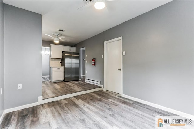 interior space featuring ceiling fan, baseboard heating, freestanding refrigerator, wood finished floors, and white cabinets