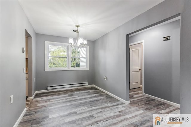 spare room featuring a baseboard heating unit, an inviting chandelier, wood finished floors, and baseboards