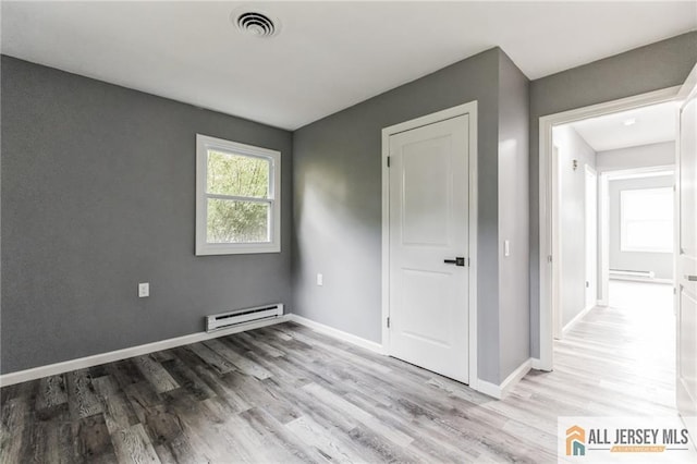 empty room with visible vents, wood finished floors, baseboards, and a baseboard radiator