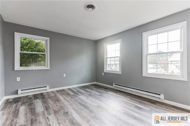 spare room featuring visible vents, plenty of natural light, and a baseboard heating unit