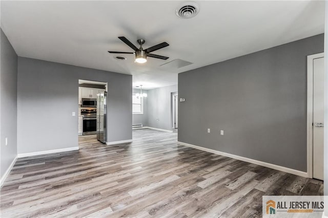 empty room with wood finished floors, ceiling fan with notable chandelier, visible vents, and baseboards