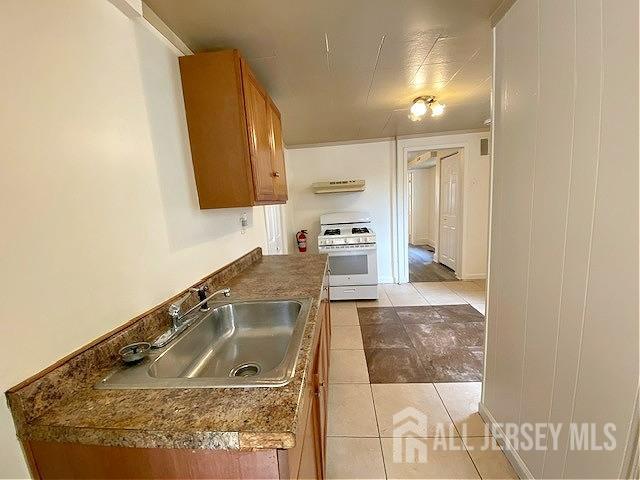 19 Haag St, Sayreville, NJ 08872 - kitchen with white gas stove, brown cabinetry, ventilation hood, light tile patterned floors, and dark countertops
