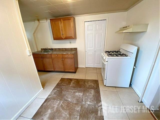 19 Haag St, Sayreville, NJ 08872 - kitchen with white range with gas cooktop, under cabinet range hood, brown cabinetry, and dark countertops