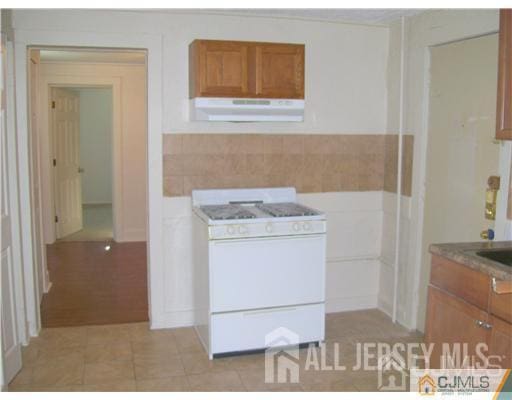 19 Haag St, Sayreville, NJ 08872 - kitchen with under cabinet range hood, white gas stove, brown cabinets, wainscoting, and light tile patterned floors