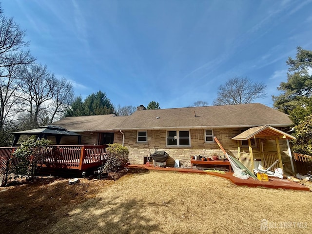 rear view of property with a chimney, a shingled roof, stone siding, a gazebo, and a deck