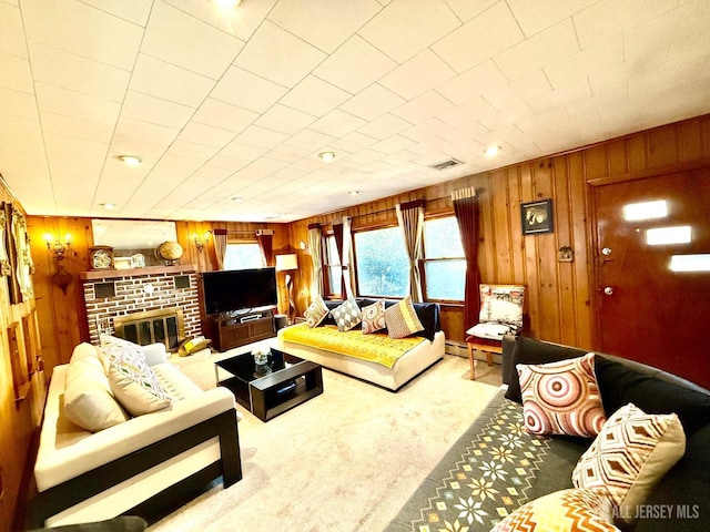 carpeted living room featuring a baseboard heating unit, wood walls, a brick fireplace, and visible vents