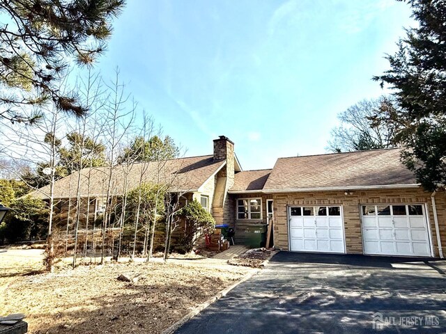 view of front facade with a shingled roof, driveway, a chimney, and a garage