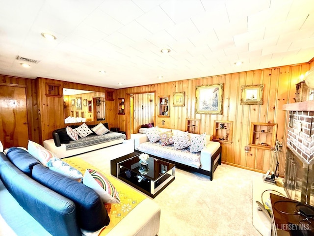 carpeted living area with visible vents, wood walls, and a brick fireplace