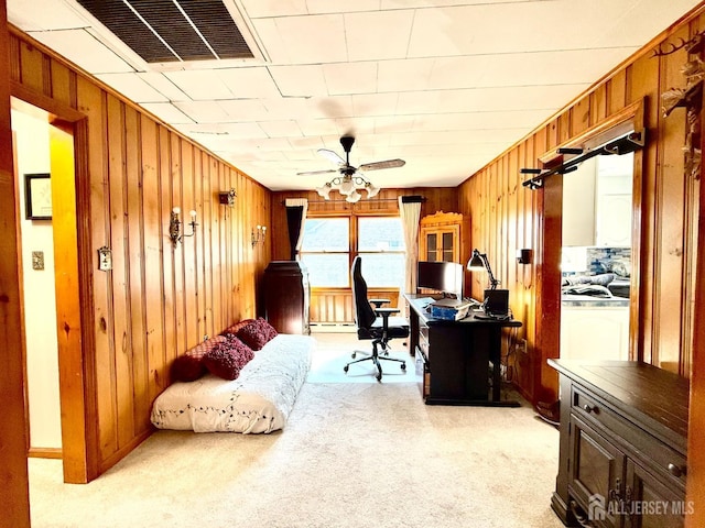 home office with wooden walls, visible vents, a ceiling fan, and light colored carpet