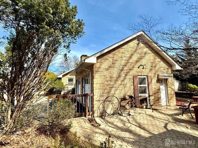 view of side of home with a chimney, brick siding, and a patio