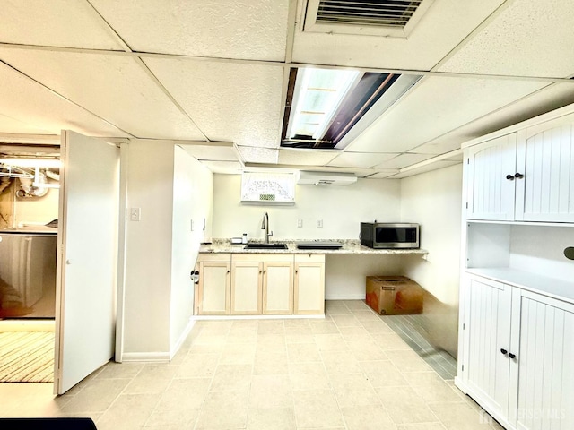 kitchen with stainless steel microwave, light countertops, a paneled ceiling, and a sink