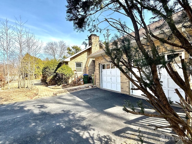 view of property exterior with a garage, stone siding, a chimney, and aphalt driveway