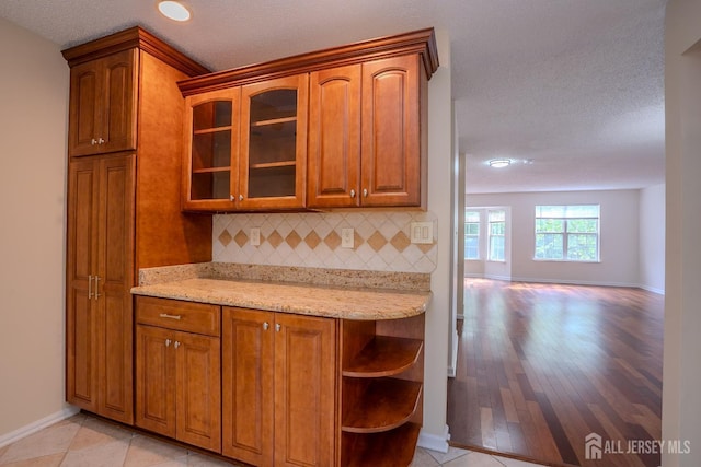 85 W Shrewsbury Pl, Princeton, NJ 08540 - kitchen with baseboards, decorative backsplash, glass insert cabinets, light stone counters, and brown cabinetry