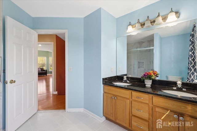 bathroom featuring a sink, baseboards, a shower stall, and double vanity