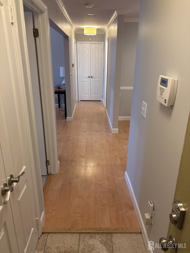 corridor with ornamental molding, baseboards, and light wood-type flooring