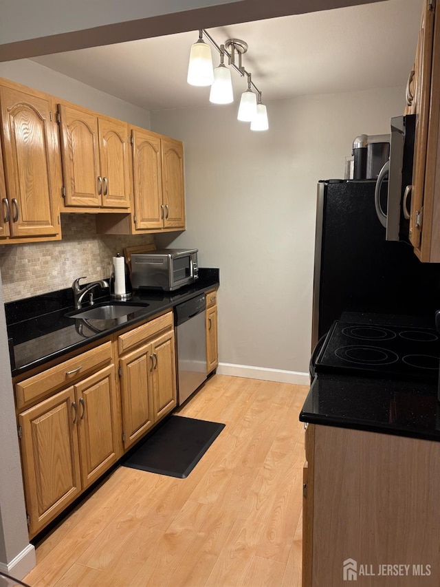 kitchen with appliances with stainless steel finishes, a sink, dark countertops, light wood-style flooring, and tasteful backsplash