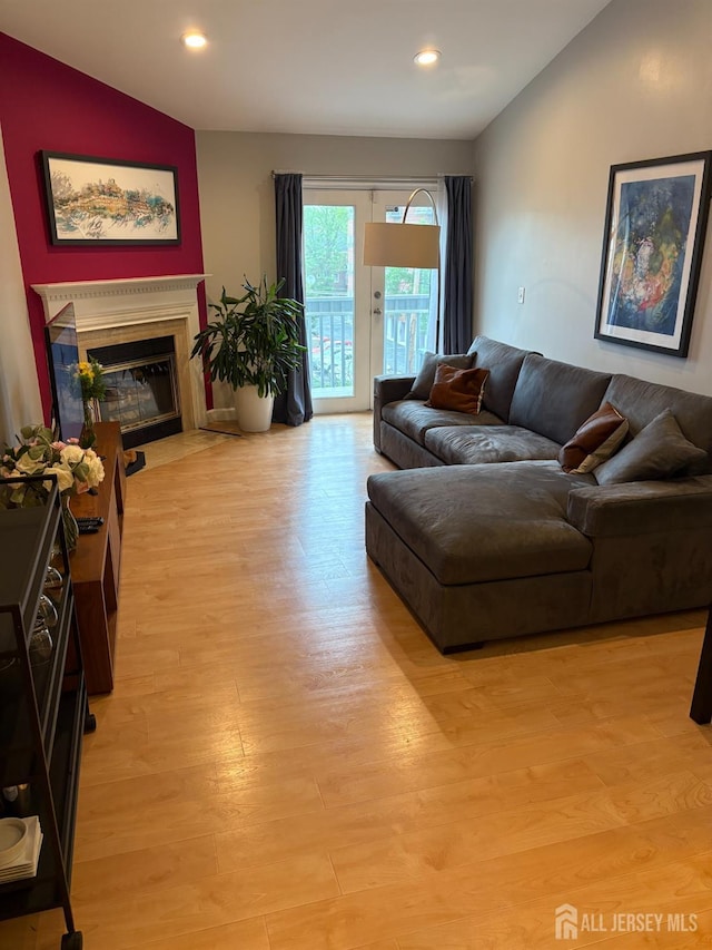living area featuring lofted ceiling, light wood-style flooring, a fireplace with flush hearth, and recessed lighting